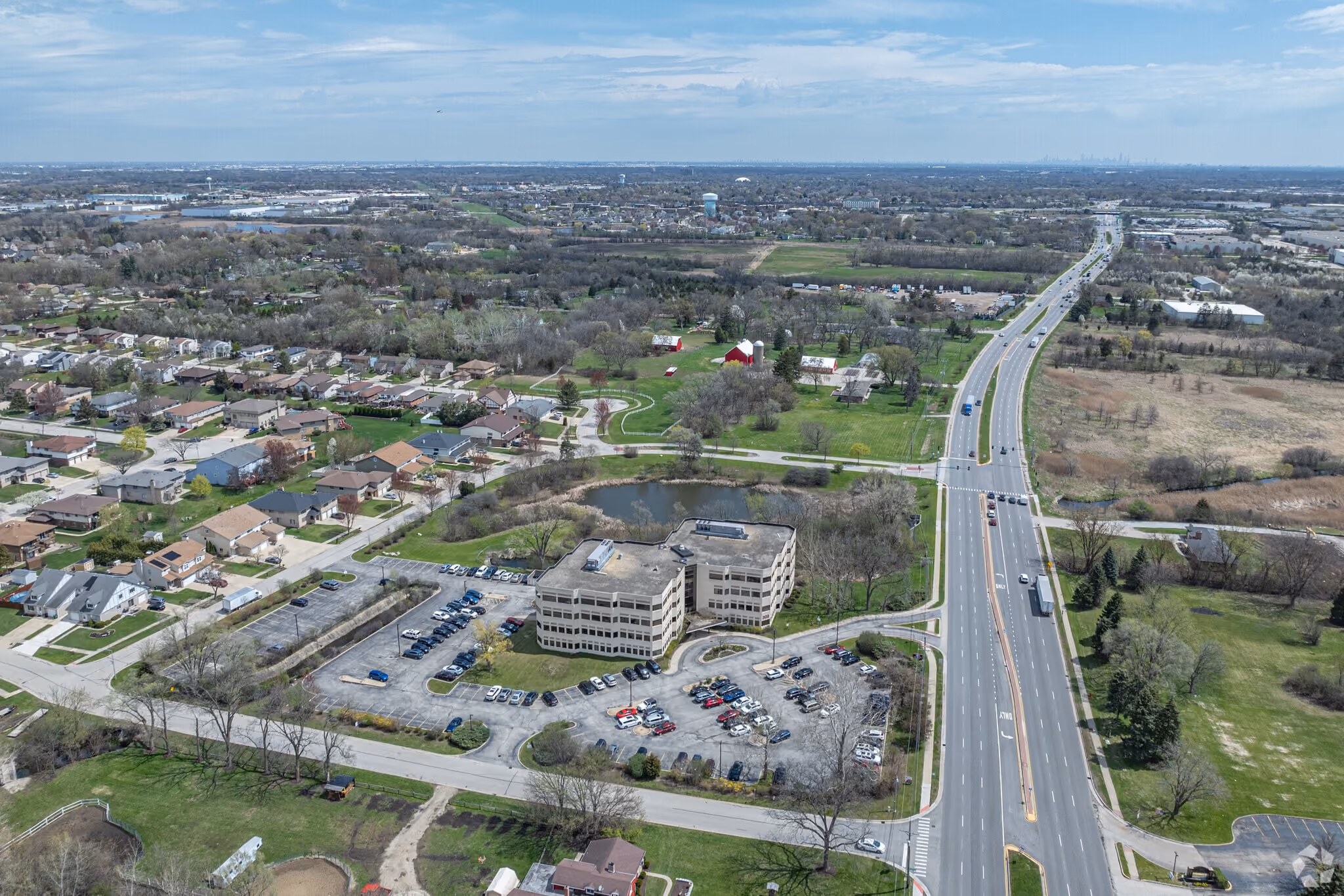 Aerial view of Willowlake at 303 East Army Trail Road, a 4-story office building beside its pond, with East Army Trail Road running past it toward the Chicago skyline on the horizon